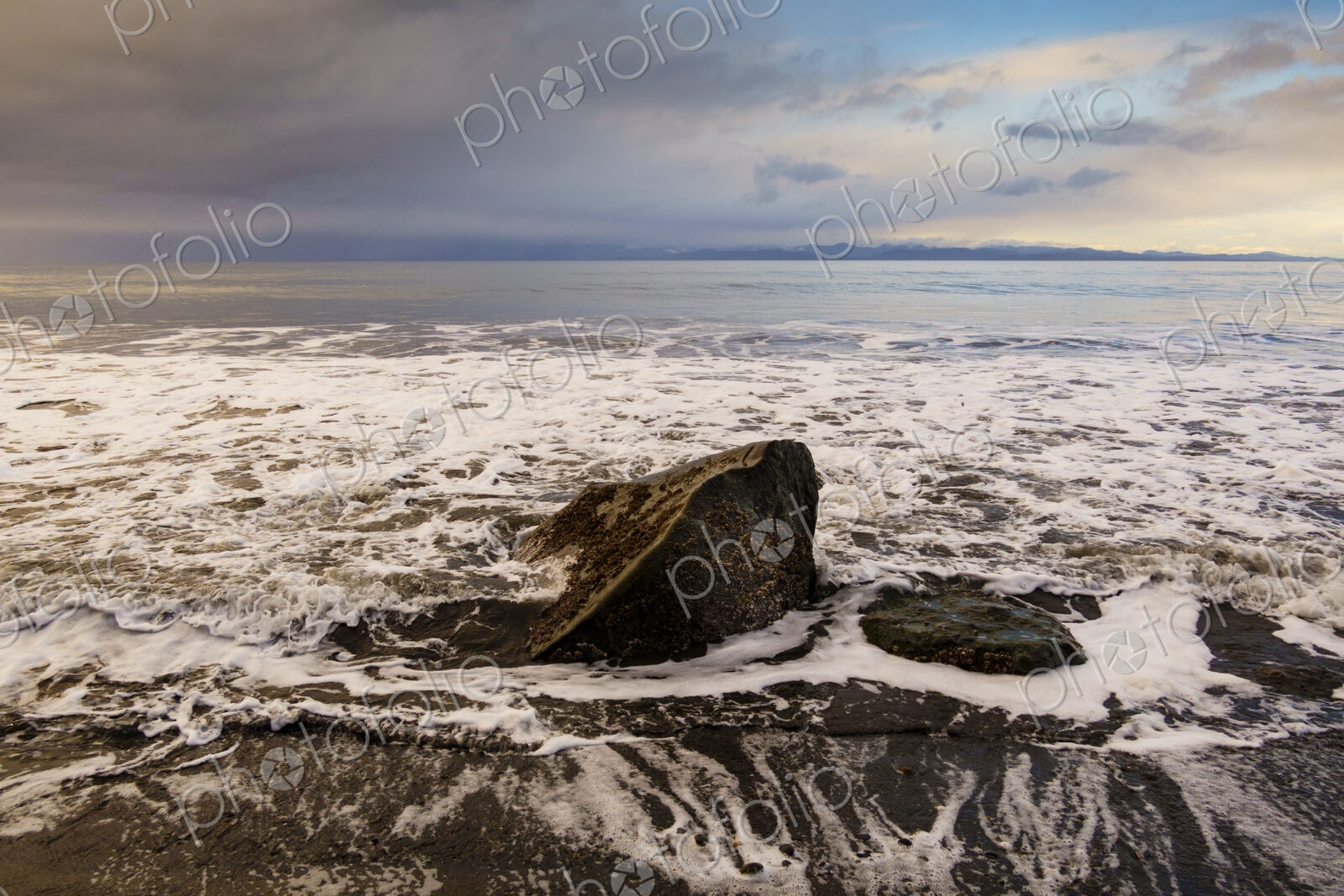 Waves surrounding boulder on beach along the Strait of Juan de Fuca, Port Angeles, WA USA