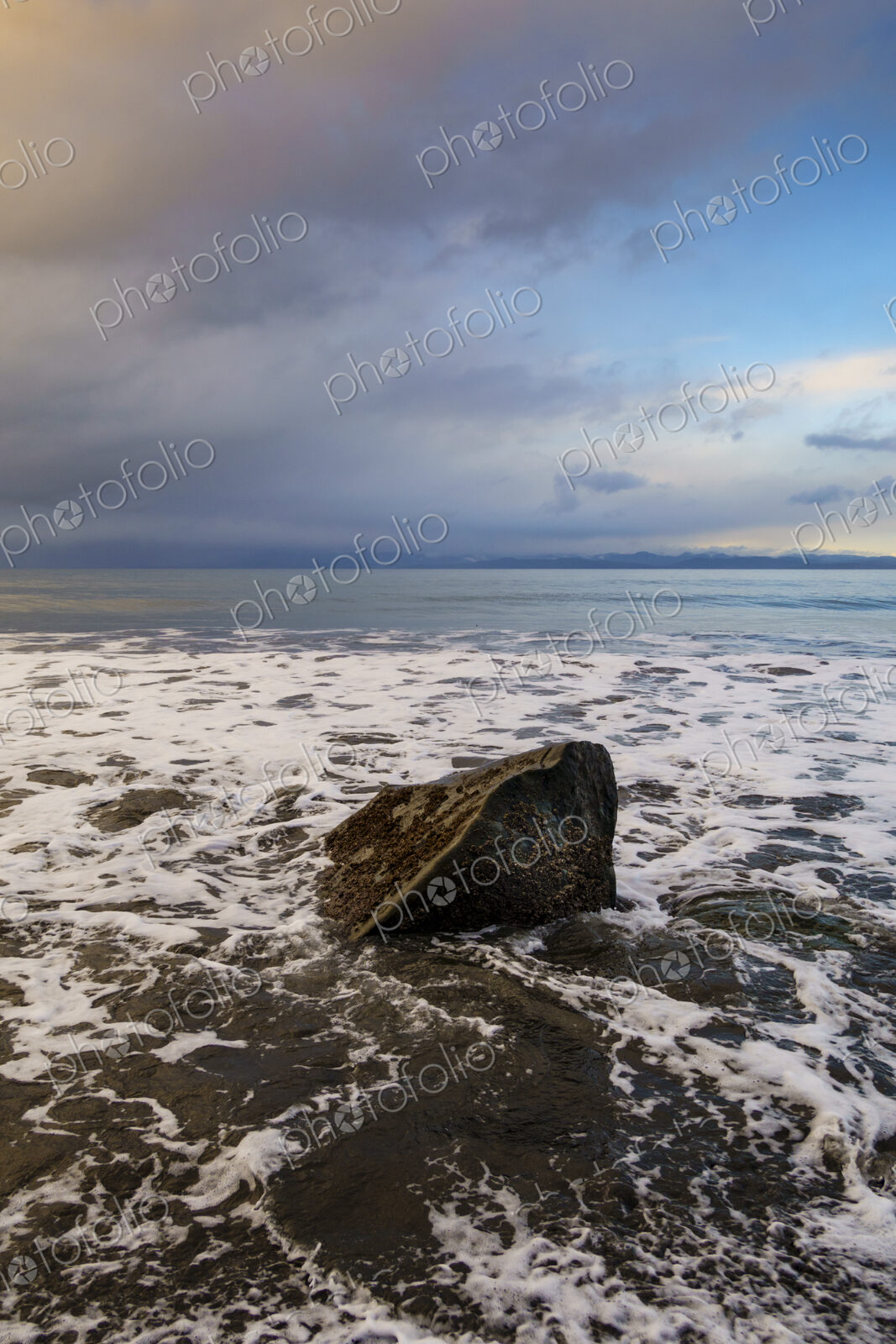 Waves surrounding boulder on beach along the Strait of Juan de Fuca, Port Angeles, WA USA