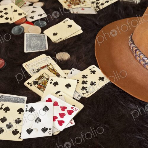 Weathered playing cards and clay chips scattered on dark animal hide beside a cowboy… Weathered playing cards and clay chips scattered on dark animal hide beside a cowboy…