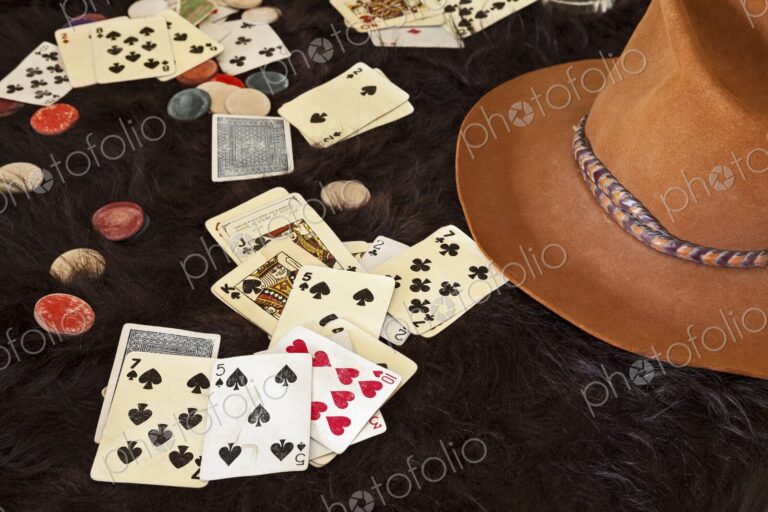 Weathered playing cards and clay chips scattered on dark animal hide beside a cowboy…