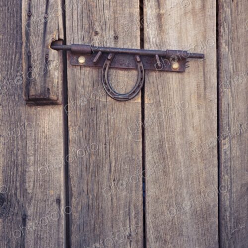 Weathered wooden door with a metal latch and horseshoe, rustic detail evoking Western… Weathered wooden door with a metal latch and horseshoe, rustic detail evoking Western…