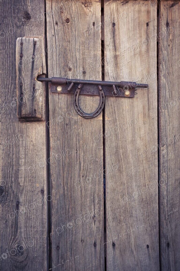 Weathered wooden door with a metal latch and horseshoe, rustic detail evoking Western…