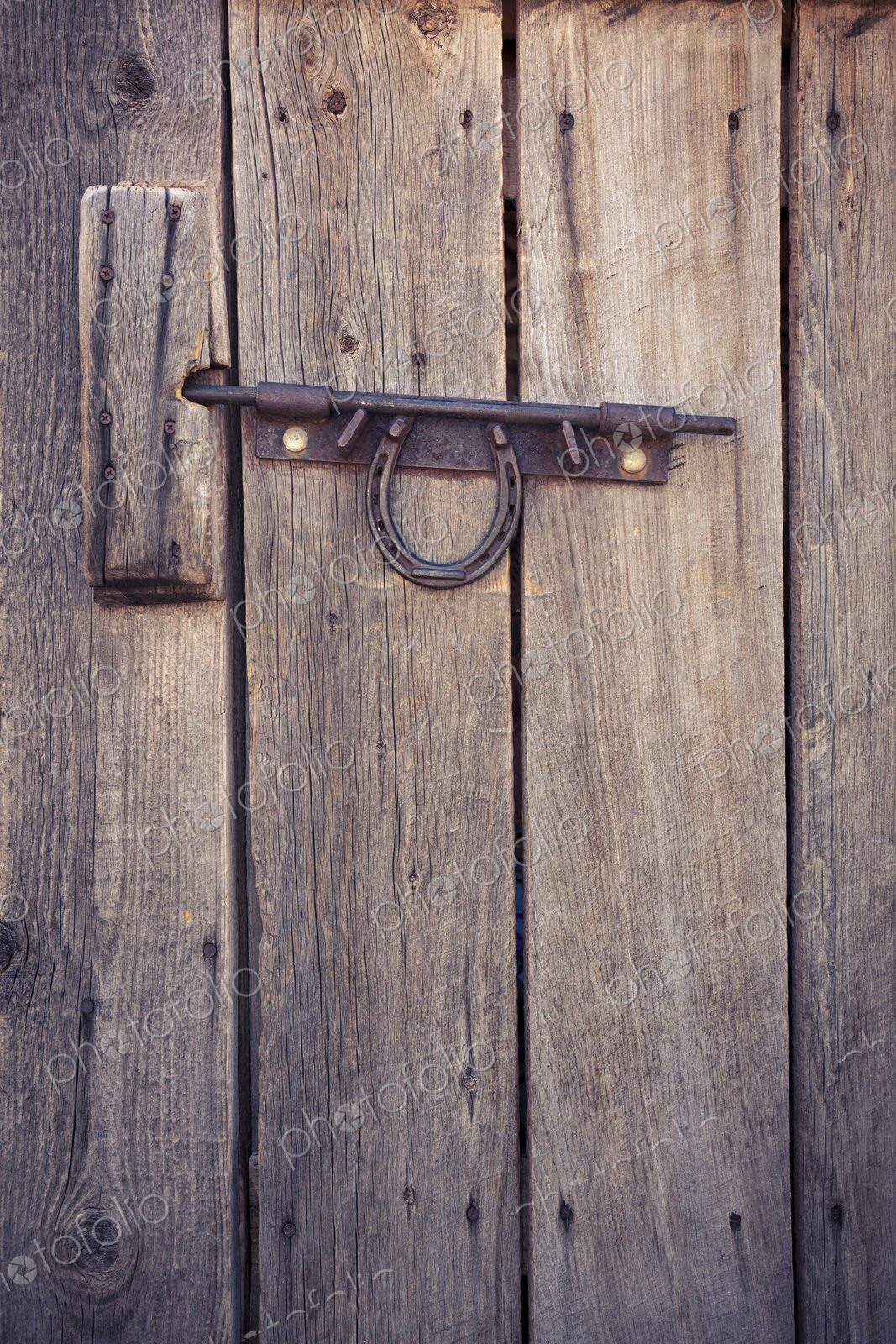 Weathered wooden door with a metal latch and horseshoe, rustic detail evoking Western…