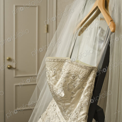 Wedding dress and veil hanging on rack in hotel room.