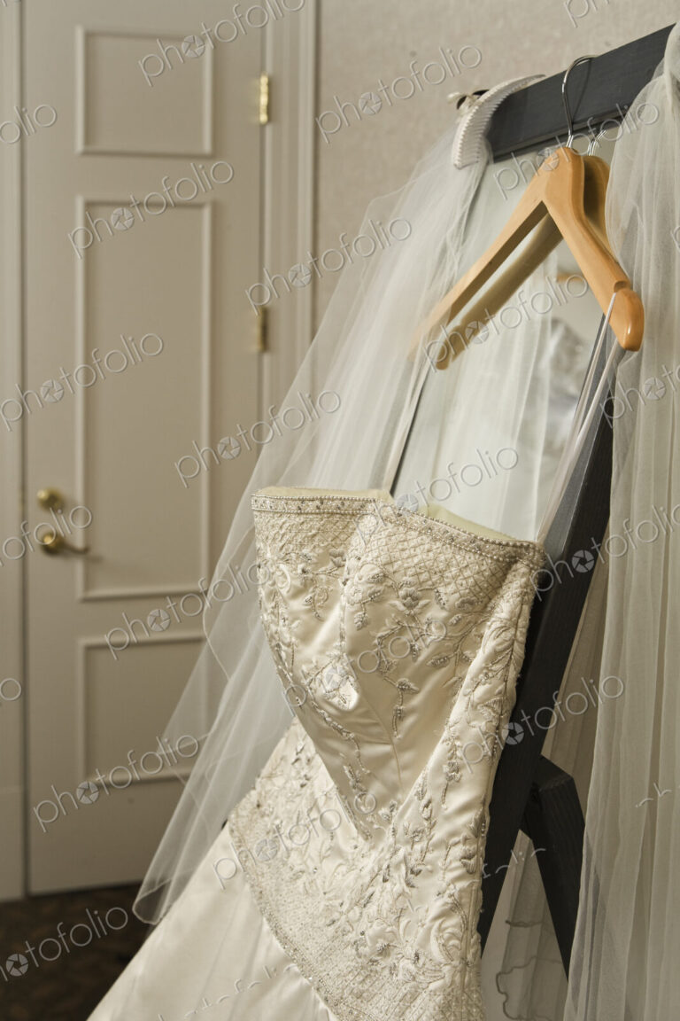 Wedding dress and veil hanging on rack in hotel room.