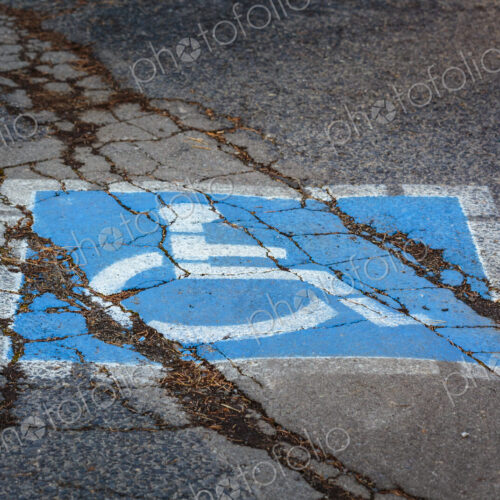 Wheelchair sign, a disabled parking spot, a blue and white sign on a cracked pavement