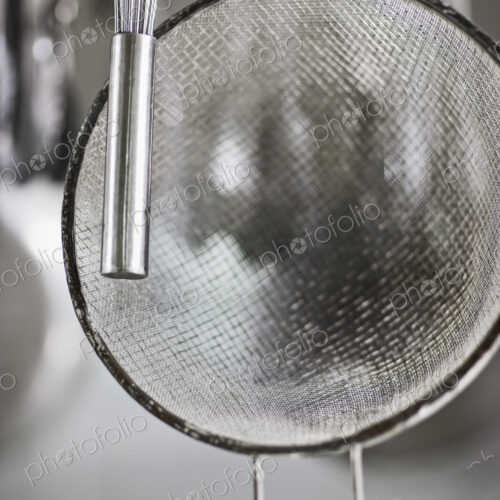 Whisk and sieve hanging in commercial kitchen. Whisk and sieve hanging in commercial kitchen.