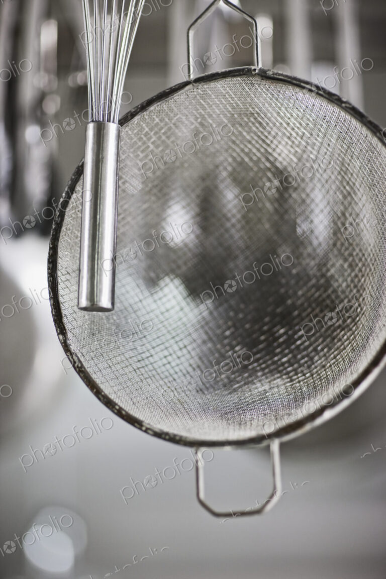 Whisk and sieve hanging in commercial kitchen.