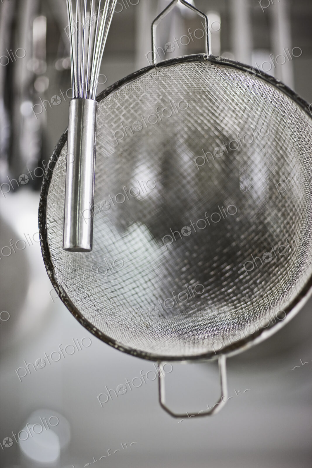 Whisk and sieve hanging in commercial kitchen.
