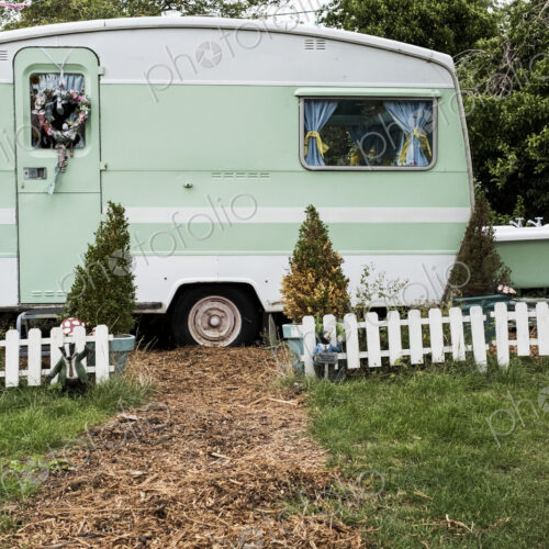 White and green retro caravan parked at the end of a garden path behind low white… White and green retro caravan parked at the end of a garden path behind low white…