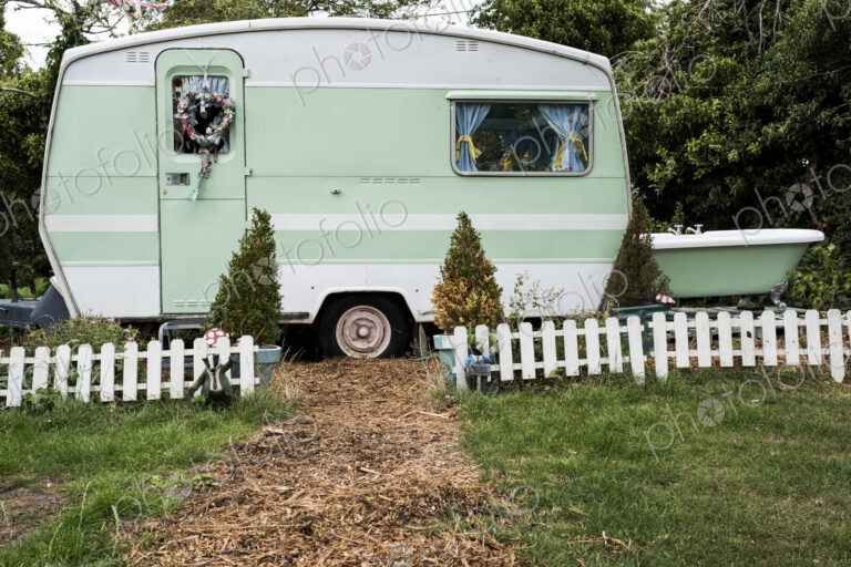 White and green retro caravan parked at the end of a garden path behind low white…