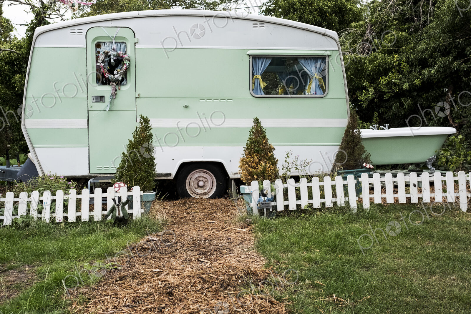 White and green retro caravan parked at the end of a garden path behind low white…