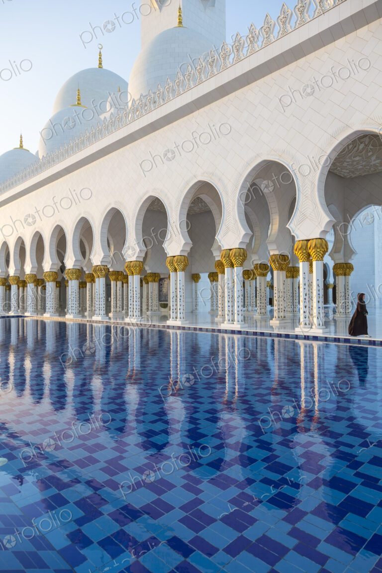 White colonnade of Sheikh Zayed Mosque and blue fountain, Abu Dhabi, United Arab Emirates.