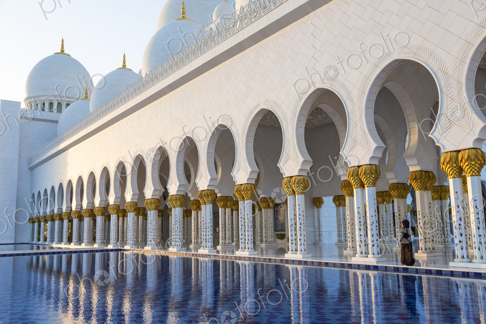 White colonnade of Sheikh Zayed Mosque and blue fountain, Abu Dhabi, United Arab Emirates.