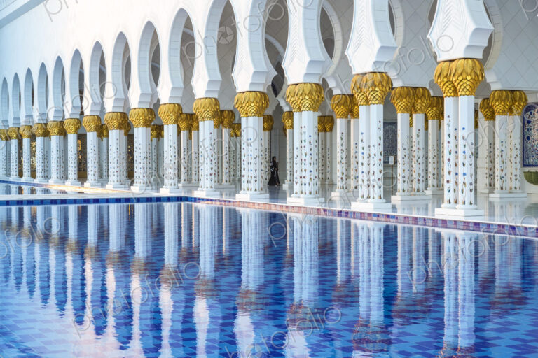 White colonnade of Sheikh Zayed Mosque and blue fountain, Abu Dhabi, United Arab Emirates.