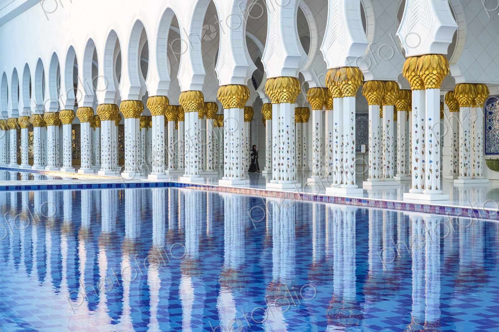 White colonnade of Sheikh Zayed Mosque and blue fountain, Abu Dhabi, United Arab Emirates.