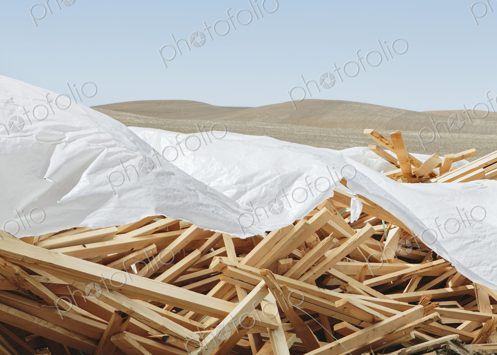 White tarp covering pile of wood 2×4 studs, farmland in background, near Pullman