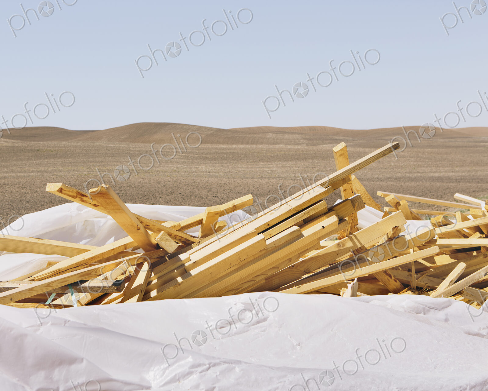 White tarp covering pile of wood 2×4 studs, farmland in background, near Pullman