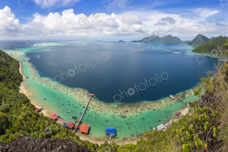 Wide angle view along coastline of tropical island, mountains in the distance.