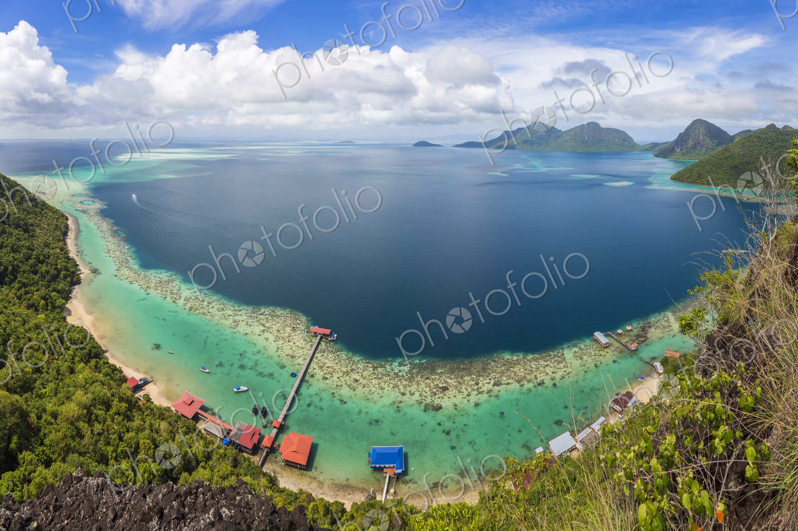 Wide angle view along coastline of tropical island, mountains in the distance.