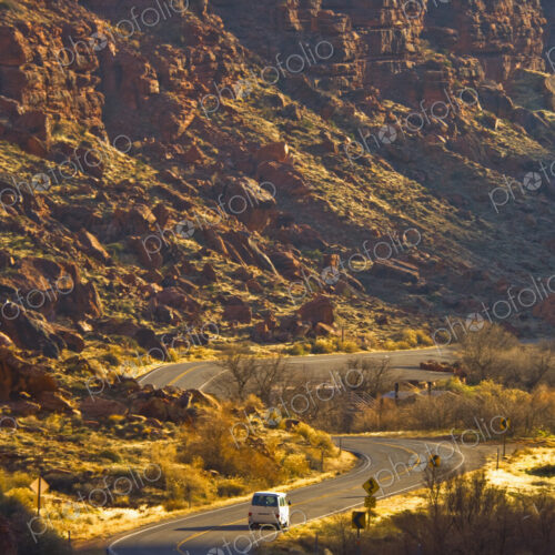 Winding road with a single car, dramatic sunlit cliffs rising from a valley Winding road with a single car, dramatic sunlit cliffs rising from a valley