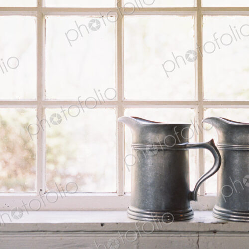 Window in historic house, hotel, two pewter jugs with handles on sill Window in historic house, hotel, two pewter jugs with handles on sill