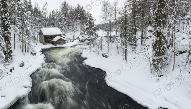 Winter landscape with log cabin and rapid in forest with snow-covered trees.