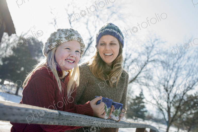 Winter scenery with snow on the ground. A child and an adult having a hot drink on a…
