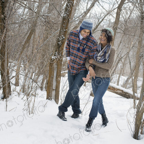Winter scenery with snow on the ground. A couple arm in arm walking through the woods.