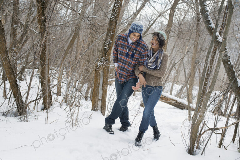 Winter scenery with snow on the ground. A couple arm in arm walking through the woods.