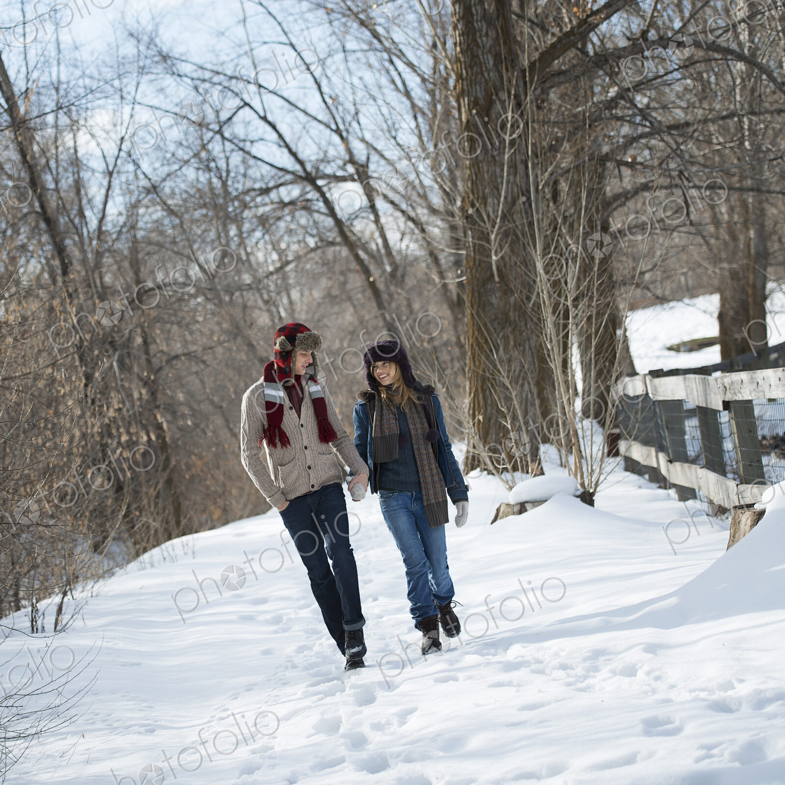 Winter scenery with snow on the ground. A couple walking hand in hand along a path.