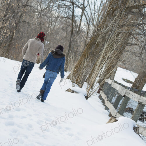 Winter scenery with snow on the ground. A couple walking hand in hand along a path.