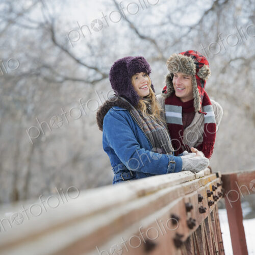 Winter scenery with snow on the ground. A couple, young man and young woman, leaning…