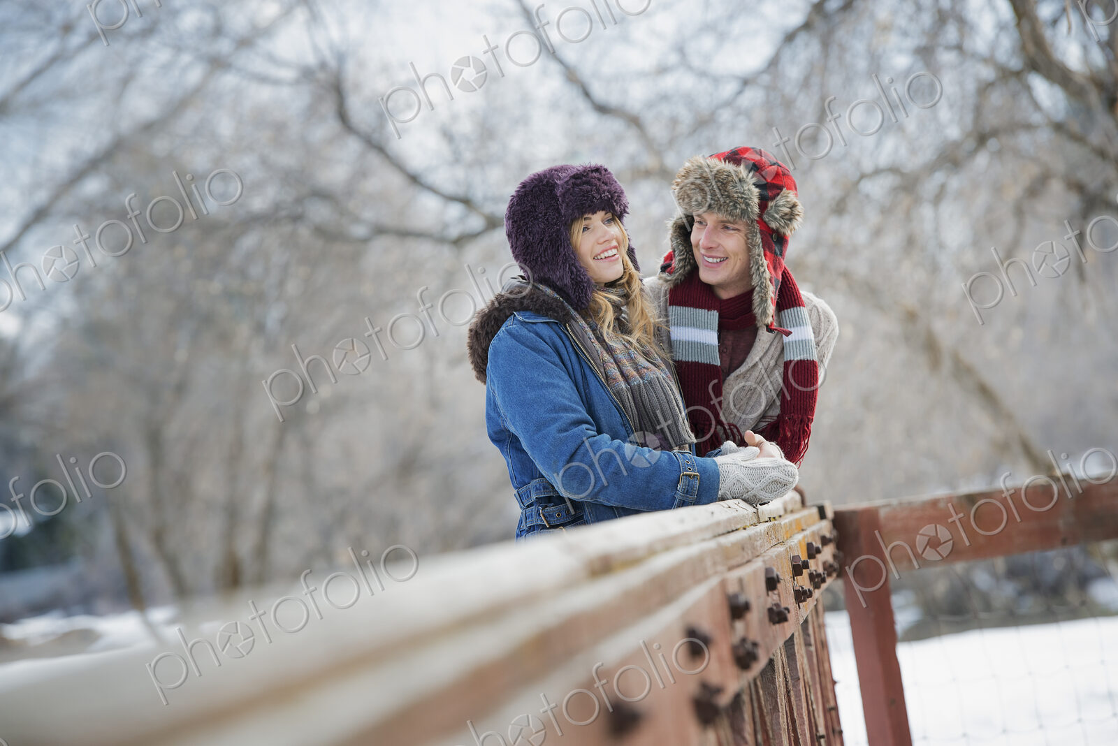 Winter scenery with snow on the ground. A couple, young man and young woman, leaning…