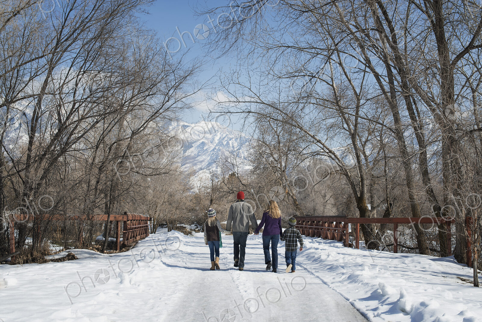 Winter scenery with snow on the ground. A family, adults and two children, walking…