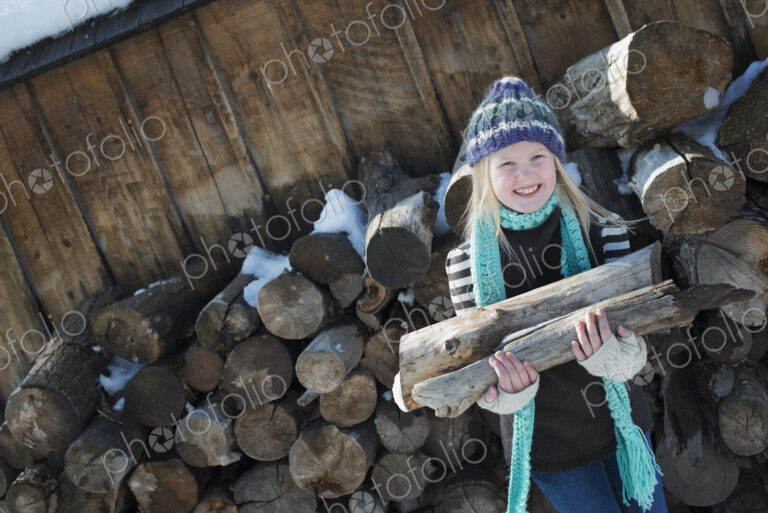Winter scenery with snow on the ground. A girl collecting firewood from the log pile.