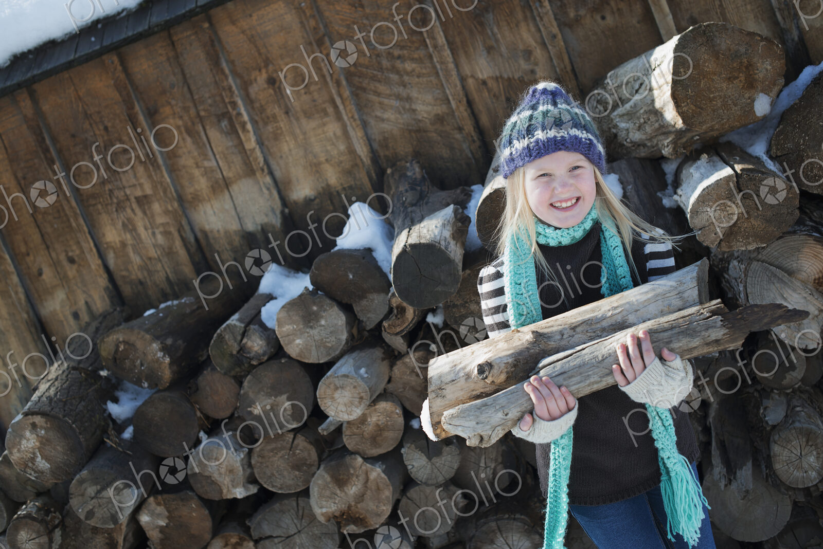 Winter scenery with snow on the ground. A girl collecting firewood from the log pile.