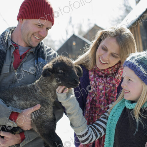 Winter scenery with snow on the ground. A man holding a young lamb, and a child… Winter scenery with snow on the ground. A man holding a young lamb, and a child…