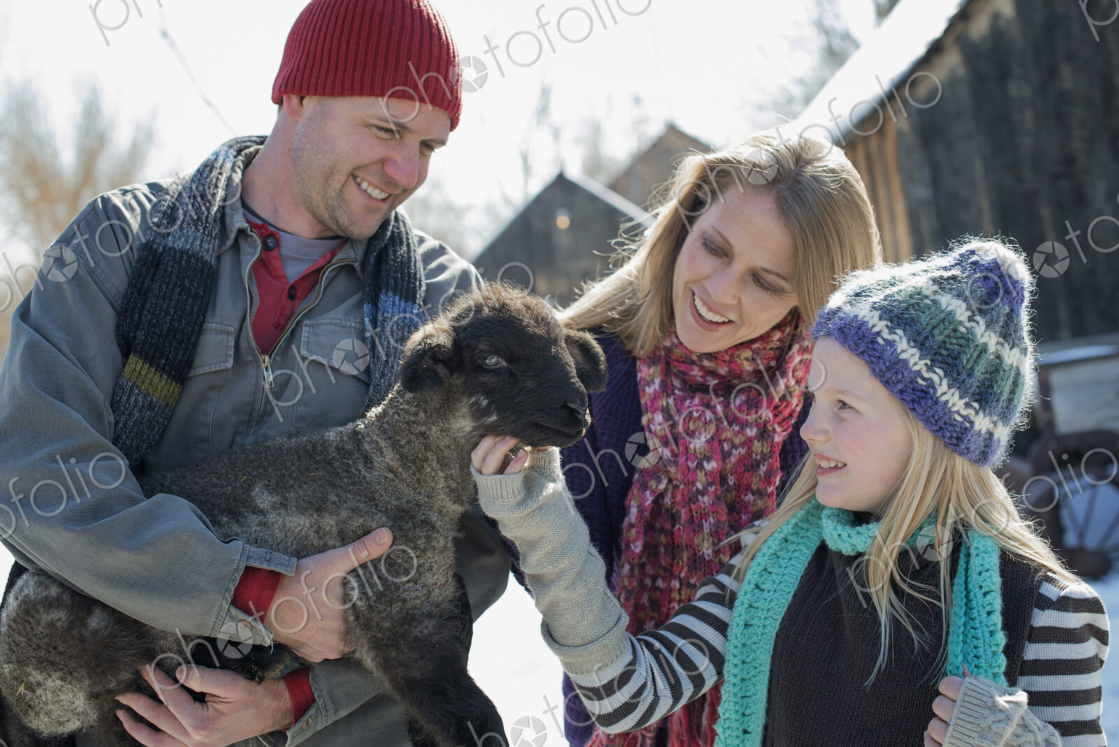 Winter scenery with snow on the ground. A man holding a young lamb, and a child…
