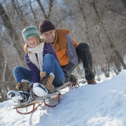 Winter scenery with snow on the ground. A man pushing a young woman from the top of a… Winter scenery with snow on the ground. A man pushing a young woman from the top of a…