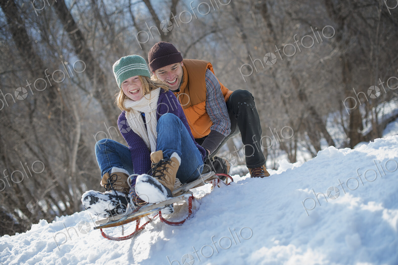Winter scenery with snow on the ground. A man pushing a young woman from the top of a…