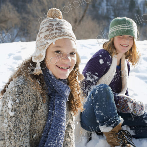 Winter scenery with snow on the ground. A woman and a child sitting on the ground…