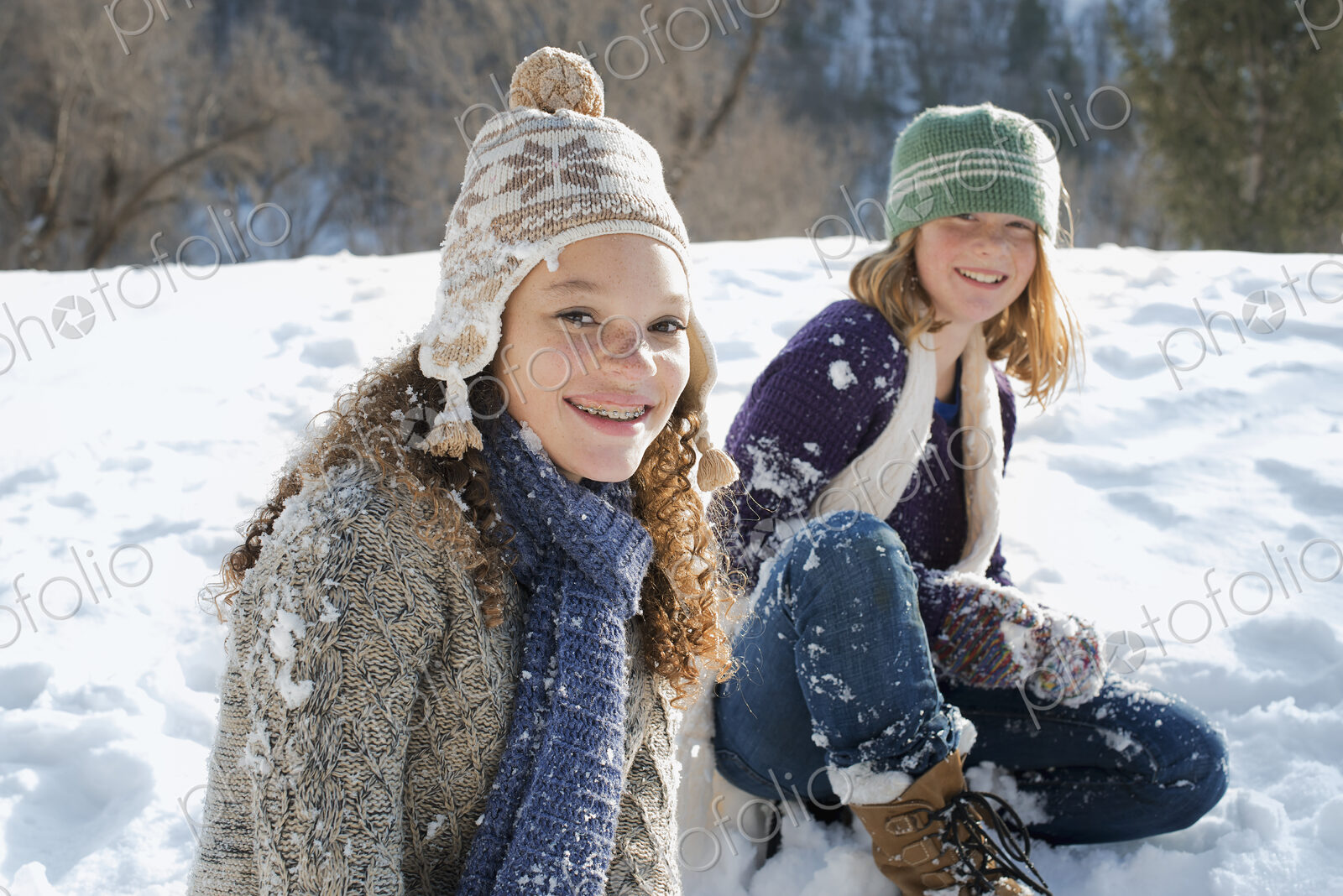 Winter scenery with snow on the ground. A woman and a child sitting on the ground…