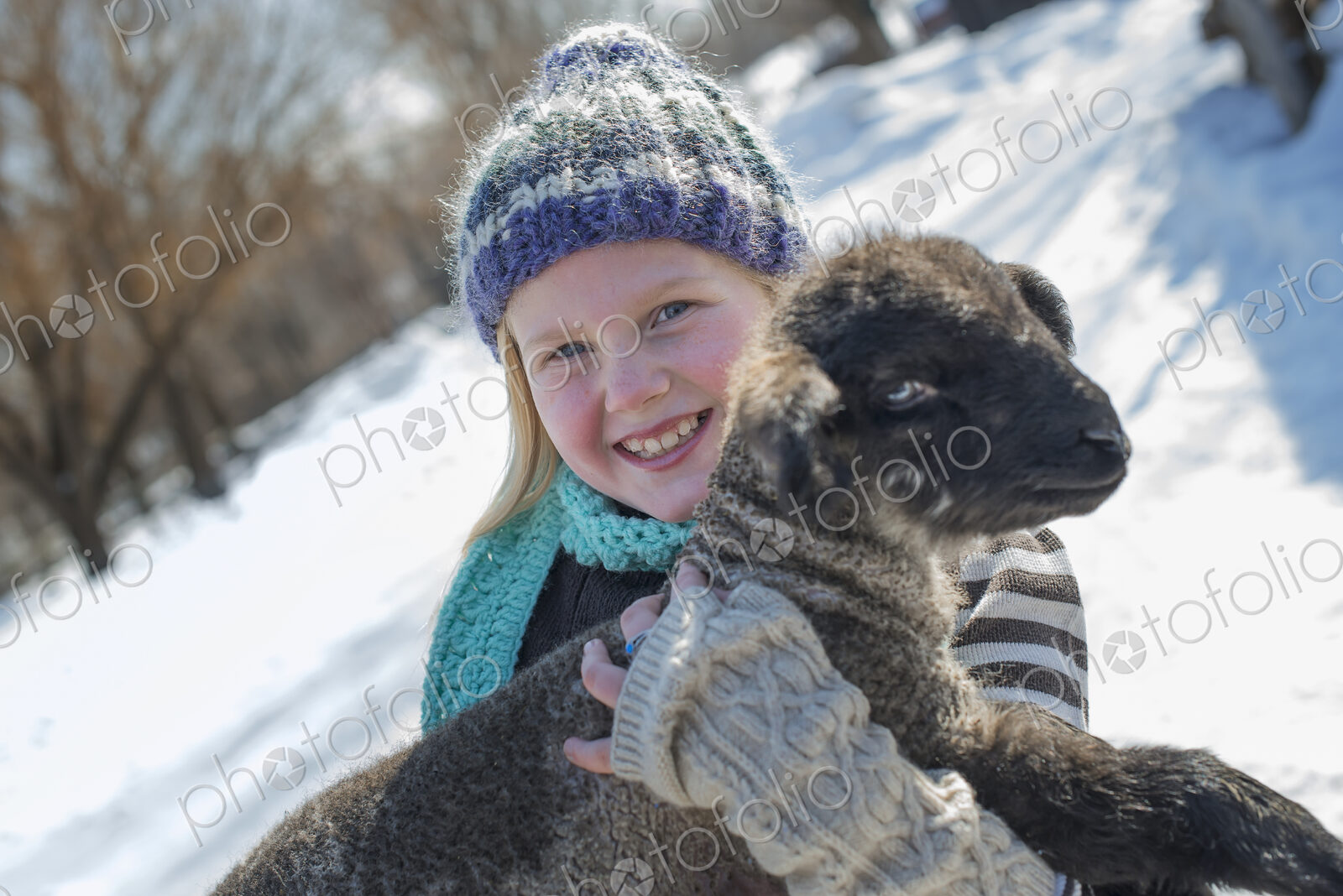 Winter scenery with snow on the ground. A young girl holding a young lamb.