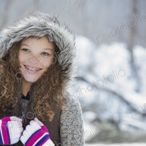 Winter scenery with snow on the ground. A young girl in a woolly hat with ski gloves on.