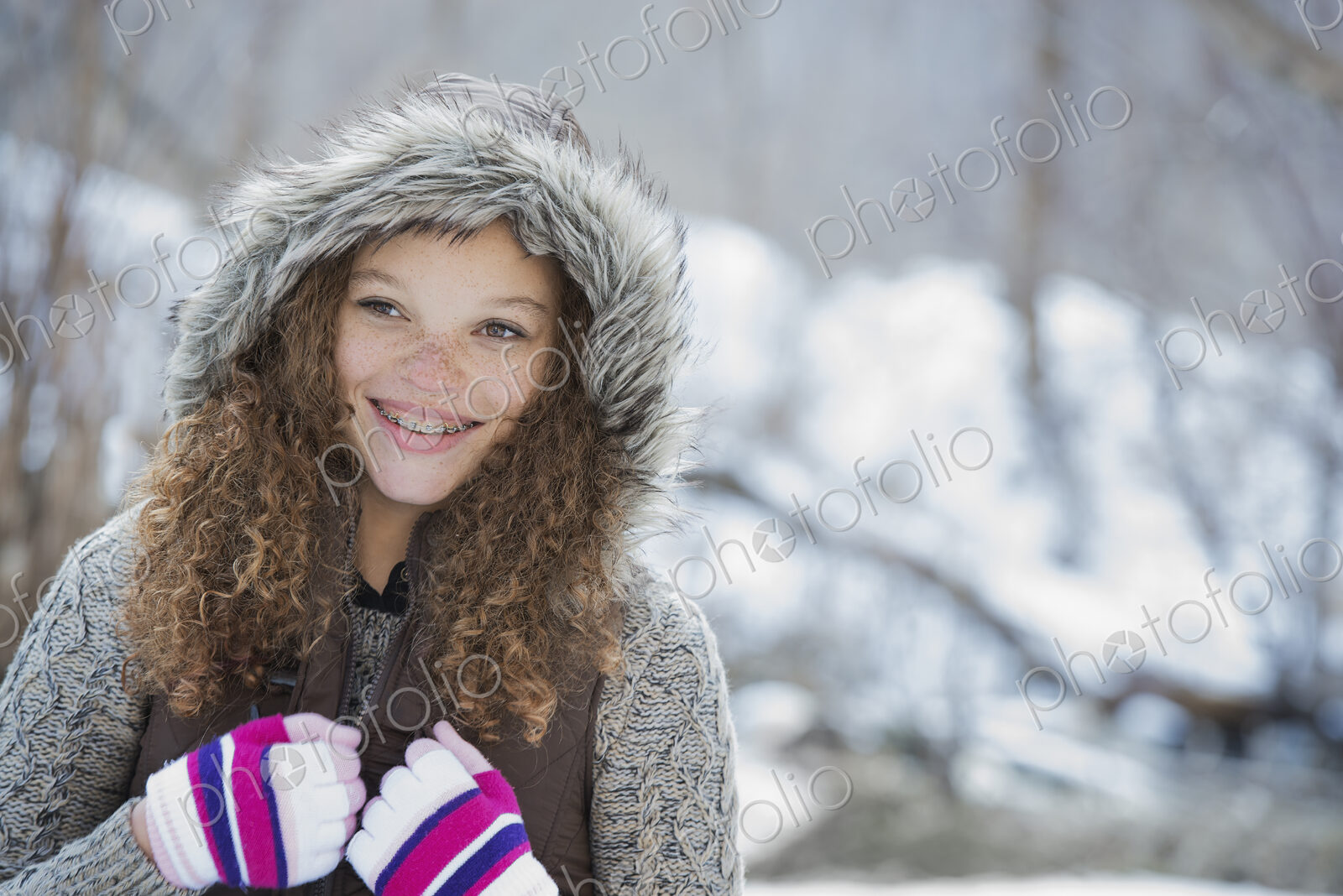 Winter scenery with snow on the ground. A young girl in a woolly hat with ski gloves on.