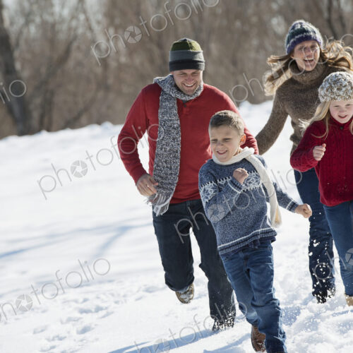 Winter scenery with snow on the ground. Family walk. Two adults chasing two children. Winter scenery with snow on the ground. Family walk. Two adults chasing two children.