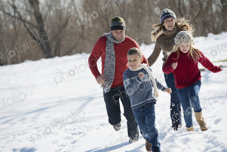 Winter scenery with snow on the ground. Family walk. Two adults chasing two children.