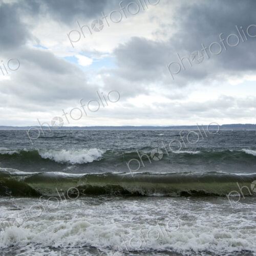 Winter, waves breaking on the shore of Puget Sound under a cloudy sky.