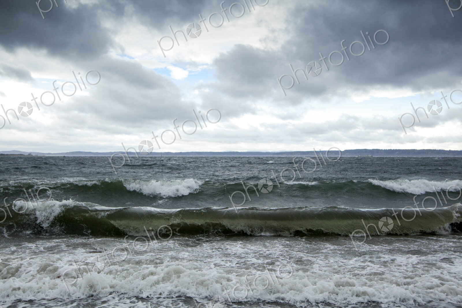 Winter, waves breaking on the shore of Puget Sound under a cloudy sky.